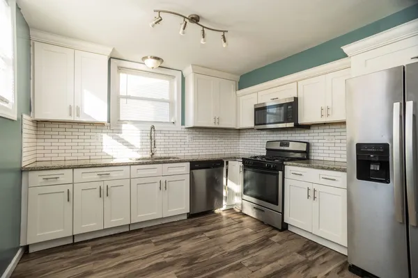 a kitchen with stainless steel appliances granite countertop a stove a sink dishwasher a refrigerator and a microwave oven with wooden floor