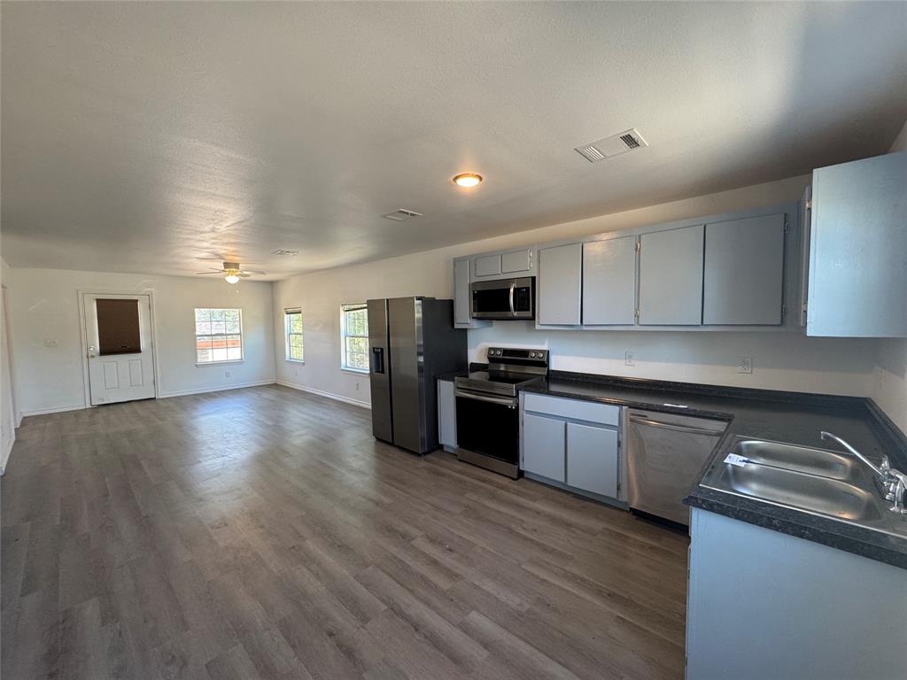 232 West Quanah Road Mabank, TX 75156 - Photo 4 of 13 Open-concept living area featuring wood-finish flooring, a ceiling fan, and multiple windows for natural light