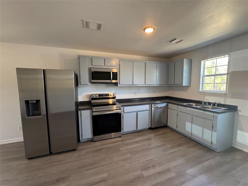 232 West Quanah Road Mabank, TX 75156 - Photo 5 of 13 Kitchen featuring L-shaped cabinetry, dark countertops, stainless steel appliances, and wood-finish flooring