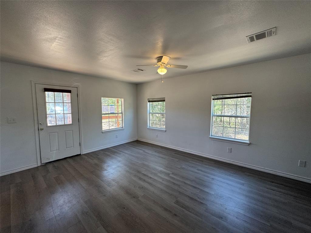 232 West Quanah Road Mabank, TX 75156 - Photo 6 of 13 Spacious room featuring wood-finish flooring, white walls, multiple windows, and a ceiling fan with integrated lighting