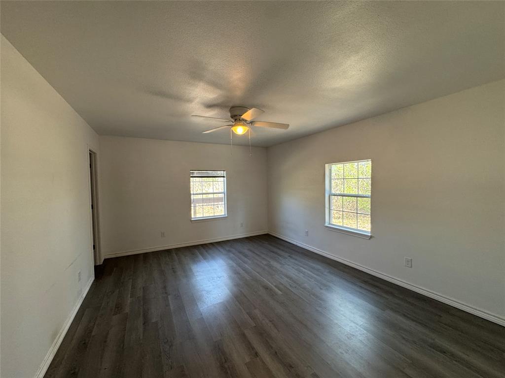 232 West Quanah Road Mabank, TX 75156 - Photo 9 of 13 Spacious room featuring wood-finish flooring, white walls, two window openings, a ceiling fan with integrated lighting, and white baseboards