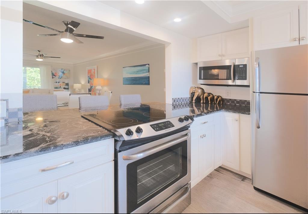 5499 Rattlesnake Hammock Road, Unit A105 Naples, FL 34113 - Photo 5 of 23 Kitchen with dark stone countertops, ornamental molding, appliances with stainless steel finishes, white cabinets, and ceiling fan