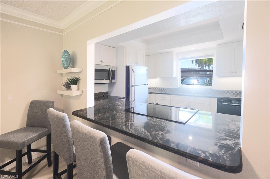 5499 Rattlesnake Hammock Road, Unit A105 Naples, FL 34113 - Photo 7 of 23 Kitchen with kitchen peninsula, a kitchen bar, black appliances, ornamental molding, and white cabinets