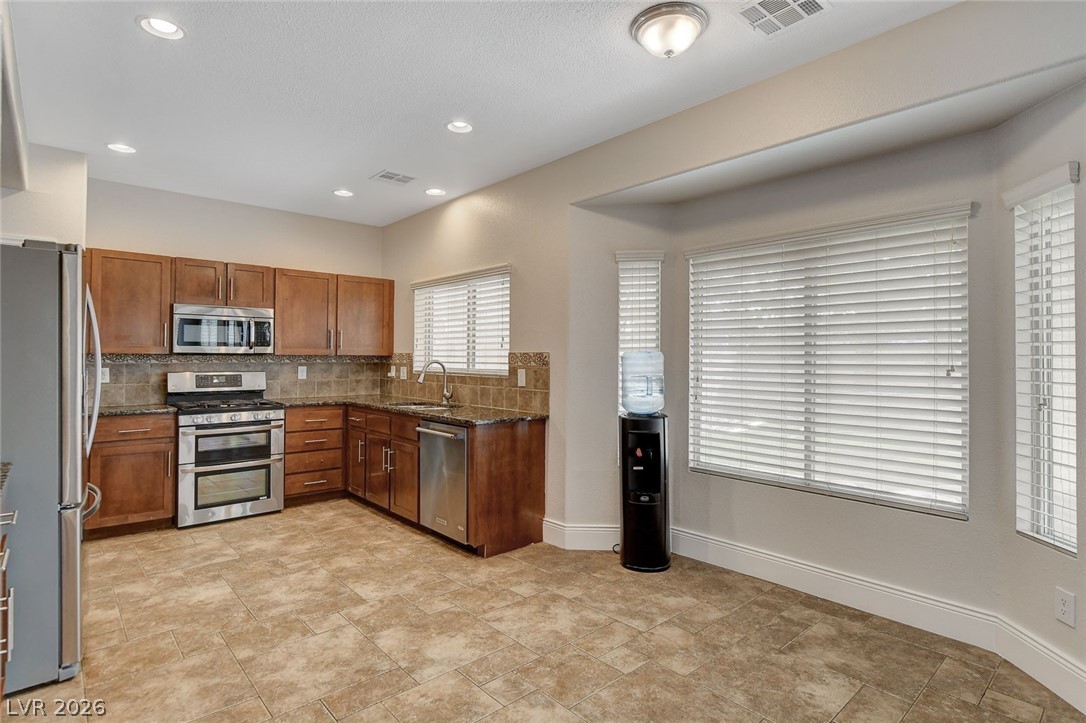 191 Verde Ridge Court Henderson, NV 89012 - Photo 17 of 36 Kitchen featuring stainless steel appliances, brown cabinets, backsplash, dark stone counters, and a sink