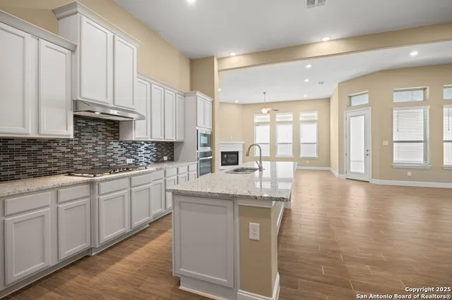 a kitchen with stainless steel appliances granite countertop a stove a sink and white cabinets with wooden floor