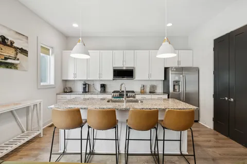 a kitchen with stainless steel appliances granite countertop a sink a stove a refrigerator and white cabinets with wooden floor