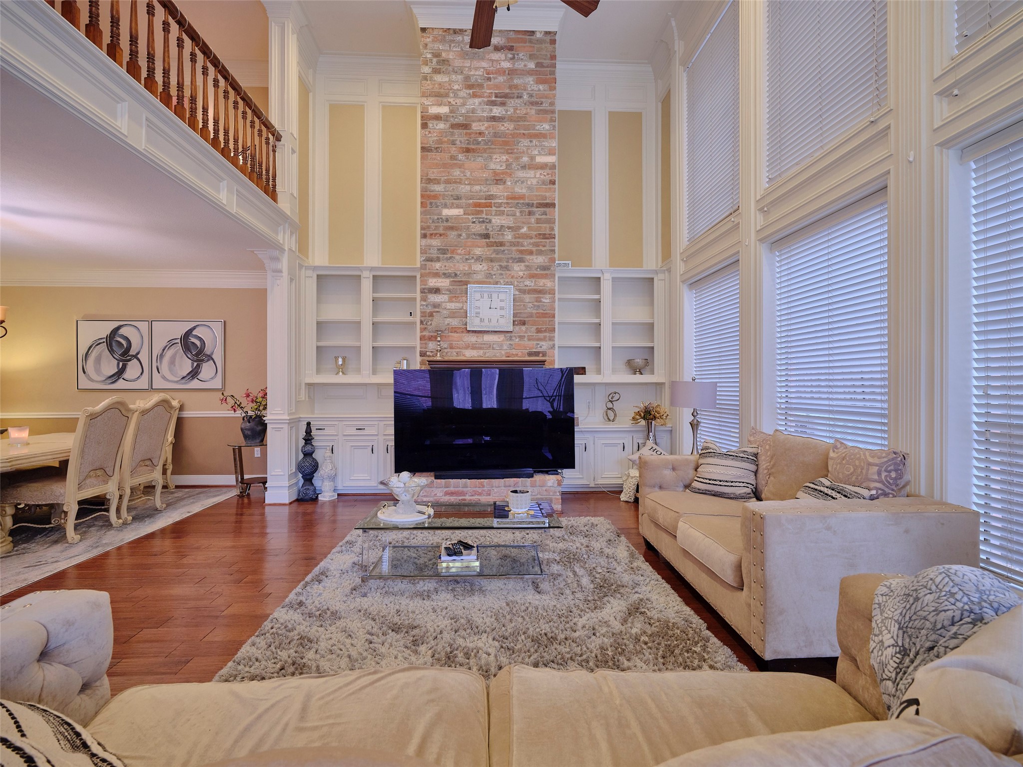 16623 Manningtree Lane Spring, TX 77379 - Photo 11 of 39 Spacious living room with a high ceiling and large windows, featuring a brick fireplace and built-in shelves. The open layout flows into a dining area, creating a warm and inviting space perfect for entertaining.
