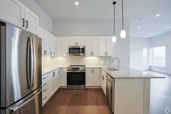 a kitchen with stainless steel appliances granite countertop a refrigerator a sink dishwasher a stove and white cabinets with wooden floor