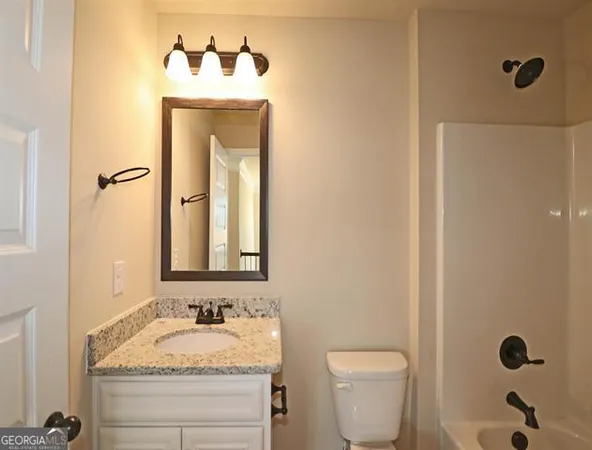a bathroom with a granite countertop sink vanity mirror and toilet