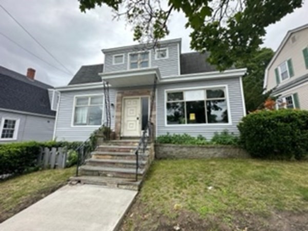 a view of a white house with large windows and a yard with plants and large trees