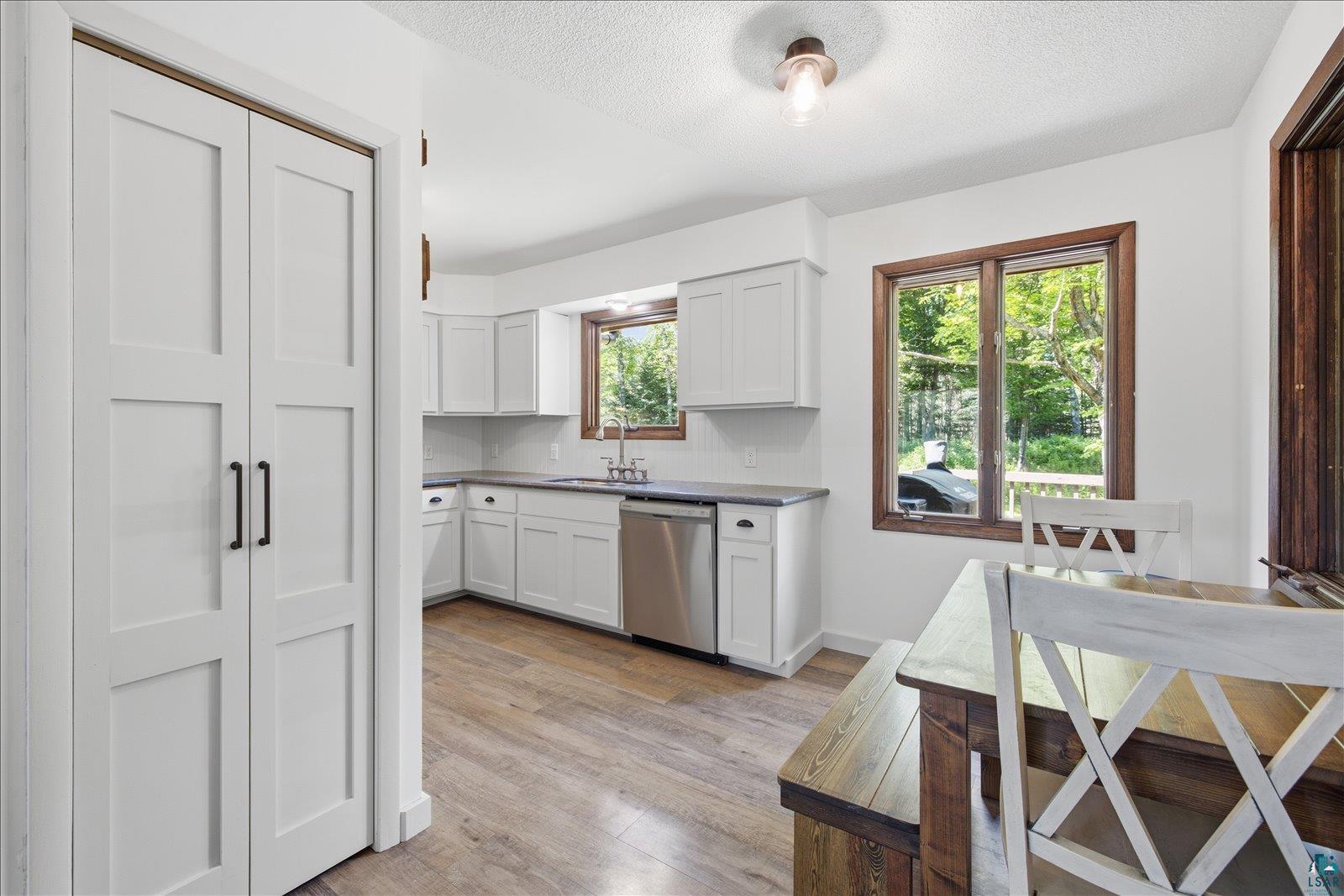 6377 Bergstrom Road Saginaw, MN 55779 - Photo 6 of 20 Modern kitchen featuring white shaker cabinetry, stainless steel dishwasher, light wood-finish flooring, and dark countertops