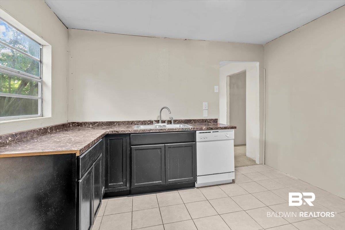 4918 Quimby Drive Mobile, AL 36619 - Photo 21 of 38 Kitchen featuring white dishwasher, a sink, dark cabinets, light tile patterned floors, and dark countertops