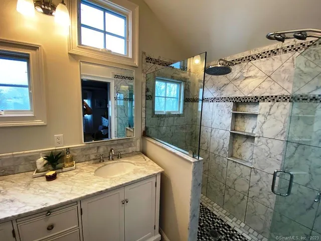 a bathroom with a granite countertop sink a mirror and shower