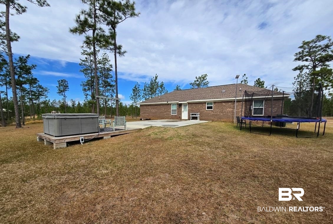 52041 Robert White Road Bay Minette, AL 36507 - Photo 2 of 16 Rear view of property featuring a lawn, a trampoline, a hot tub, and a patio
