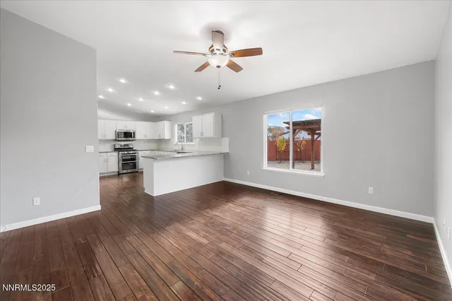 a view of an empty room with wooden floor and a kitchen
