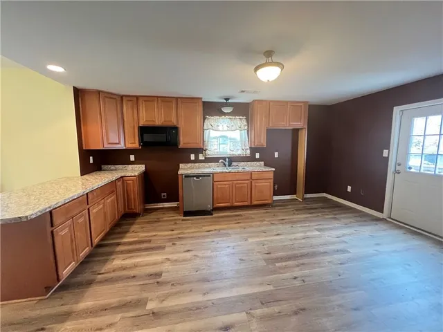 a kitchen with stainless steel appliances granite countertop a stove top oven a sink dishwasher and a refrigerator with wooden floor