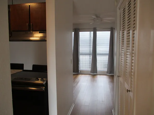 a view of a hallway to an empty room with wooden floor and a window