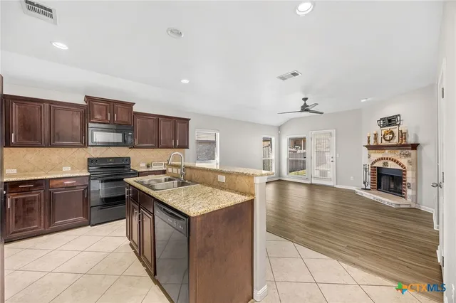 a kitchen with stainless steel appliances granite countertop a stove top oven a sink dishwasher a dining table and chairs with wooden floor