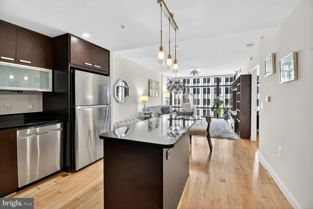 a kitchen with stainless steel appliances kitchen island granite countertop a refrigerator a sink dishwasher a dining table and chairs with wooden floor