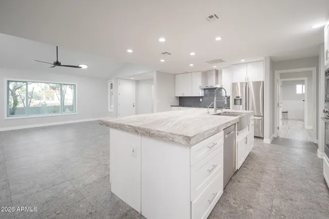 a large kitchen with a large counter top a sink stainless steel appliances and windows