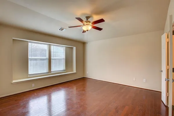 an empty room with wooden floor fan and windows