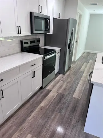 a kitchen with stainless steel appliances granite countertop a refrigerator a stove a sink and white cabinets with wooden floor