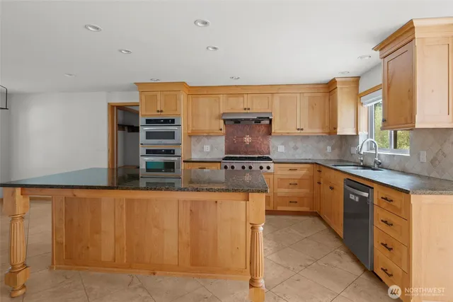 a kitchen with kitchen island granite countertop a sink cabinets stainless steel appliances and a window