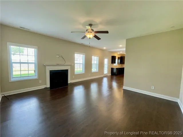 an empty room with wooden floor a ceiling fan a fireplace and windows