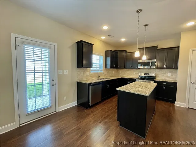 a large kitchen with stainless steel appliances kitchen island granite countertop a refrigerator a sink dishwasher a stove and a large countertops with wooden floor