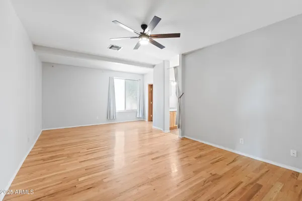 a view of an empty room with wooden floor and a ceiling fan