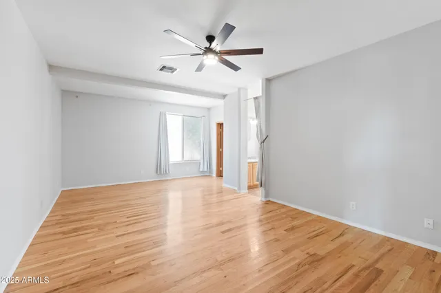 a view of an empty room with wooden floor and a ceiling fan