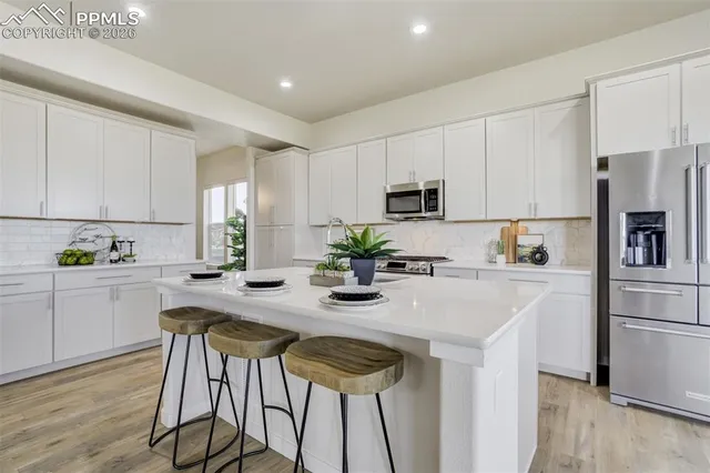 a kitchen with stainless steel appliances kitchen island granite countertop a refrigerator a stove a sink and white cabinets with wooden floor