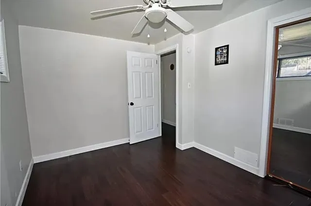 a view of an empty room with wooden floor and a ceiling fan
