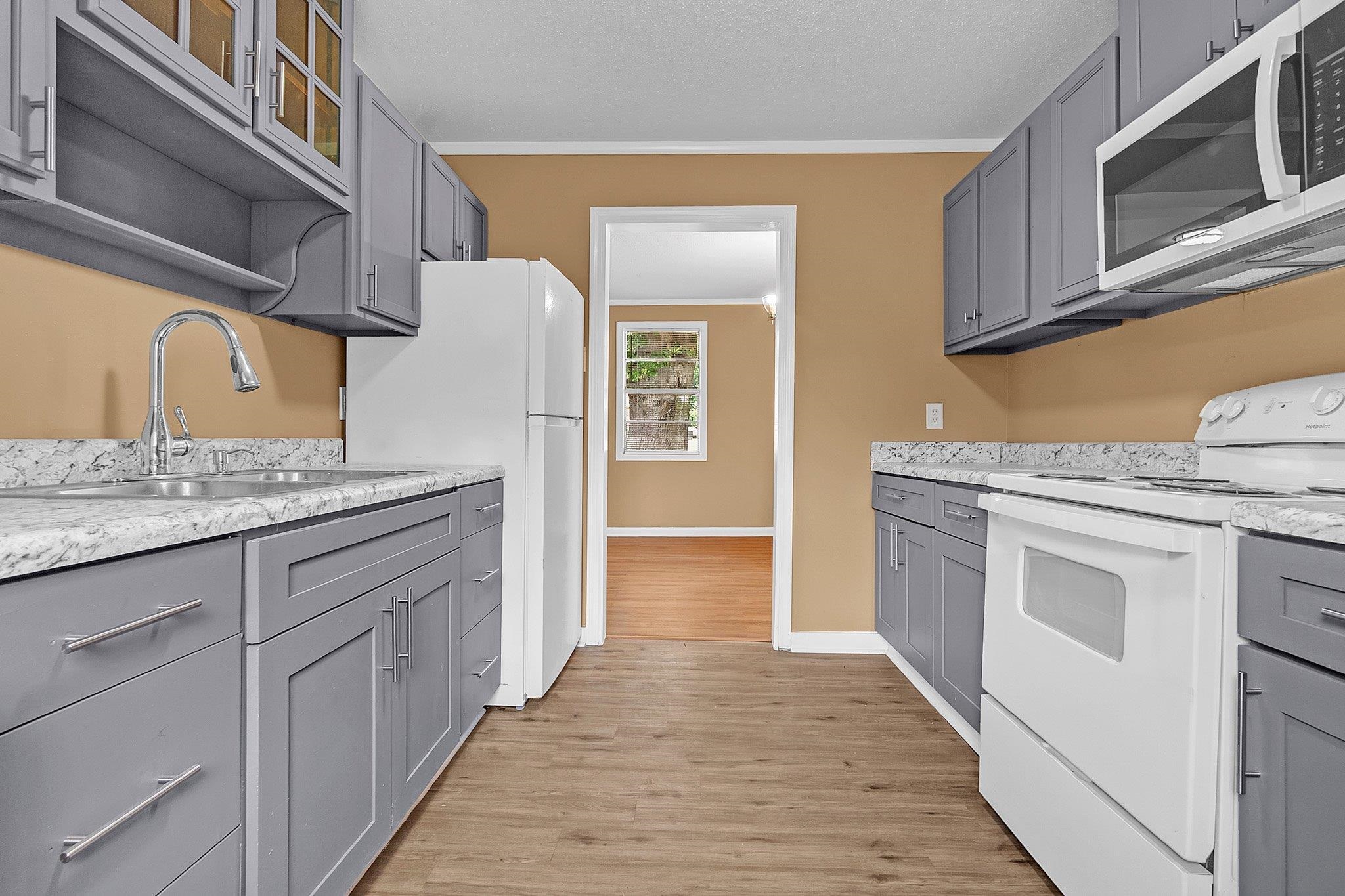 3186 Alta Road Memphis, TN 38109 - Photo 6 of 14 Kitchen featuring gray cabinetry with brushed nickel hardware, light-toned countertops, wood-finish flooring, and white appliances