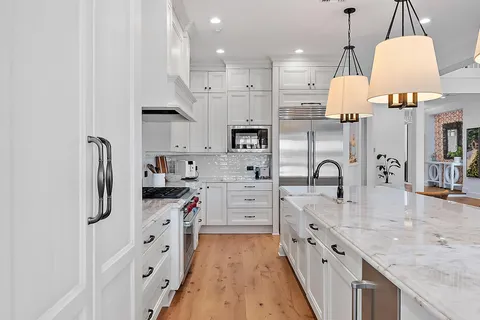 a large kitchen with stainless steel appliances kitchen island granite countertop a stove a sink a refrigerator and white cabinets with wooden floor
