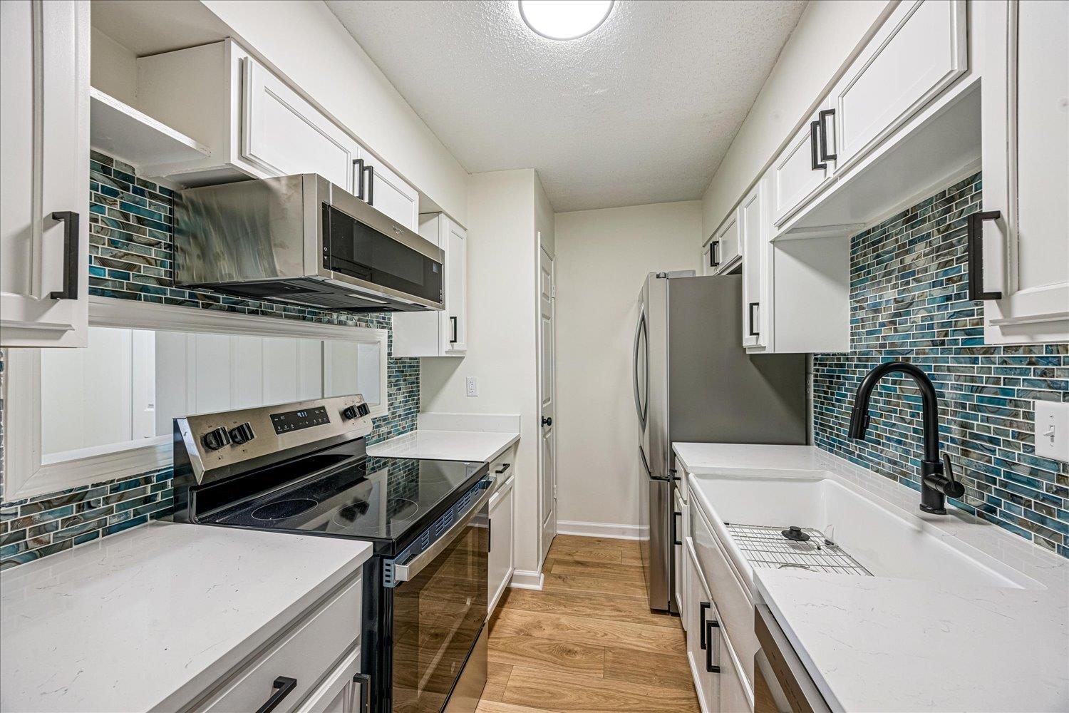 6452 Macon Road Memphis, TN 38134 - Photo 8 of 22 Kitchen featuring backsplash, appliances with stainless steel finishes, light stone countertops, light wood-type flooring, and white cabinetry