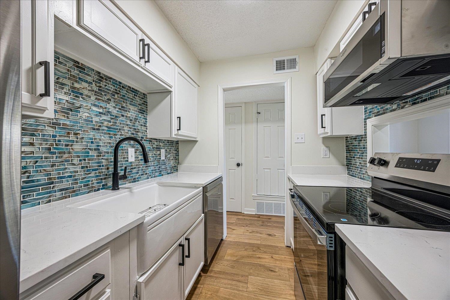 6452 Macon Road Memphis, TN 38134 - Photo 9 of 22 Kitchen featuring appliances with stainless steel finishes, light stone counters, light wood-type flooring, a textured ceiling, and white cabinets