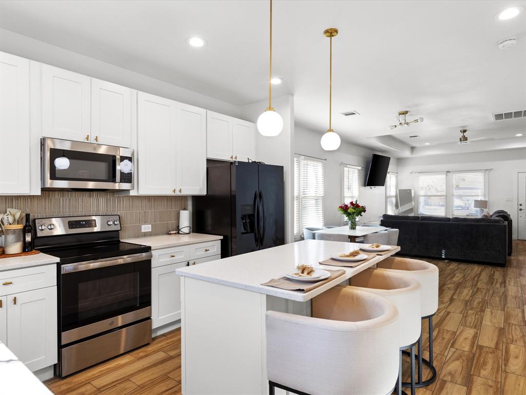 1304 East Mulkey Street Fort Worth, TX 76104 - Photo 5 of 19 a kitchen that has a sink a microwave a stove and white cabinets with wooden floor