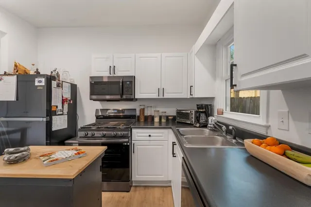 a kitchen with stainless steel appliances a stove a sink dishwasher a refrigerator white cabinets and wooden floor