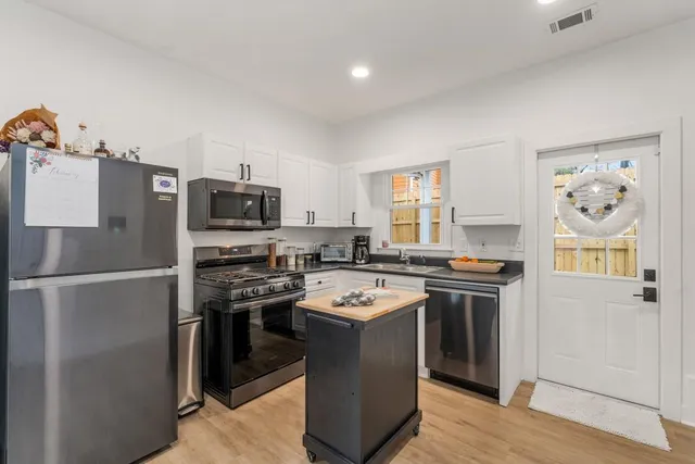 a kitchen with stainless steel appliances granite countertop a stove top oven a refrigerator a sink and dishwasher with wooden floor