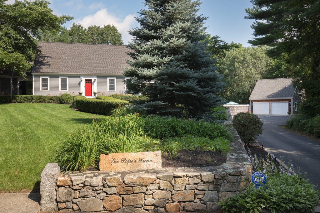 a view of a brick house with a yard plants and large tree