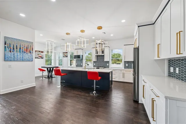 a room with stainless steel appliances kitchen island granite countertop a refrigerator a stove and white cabinets with wooden floor