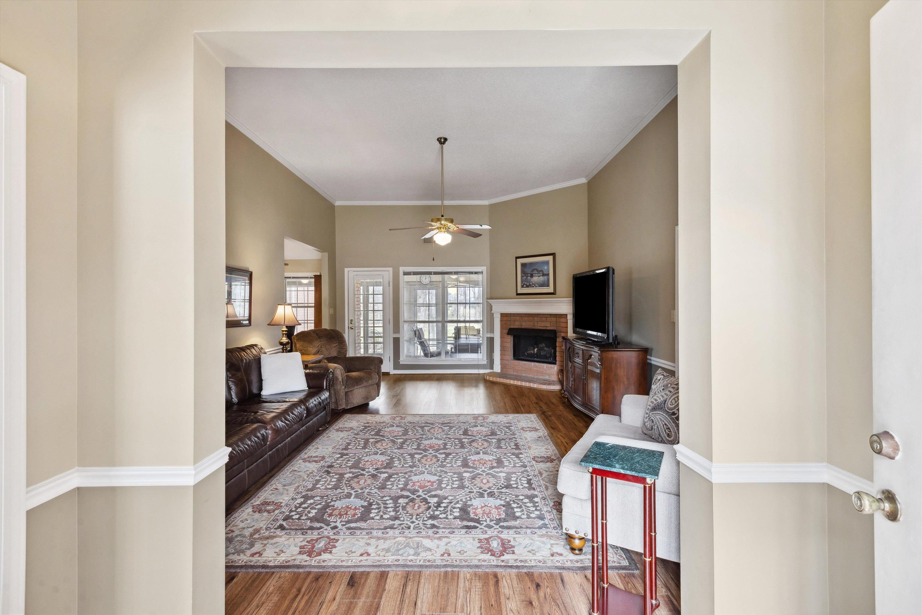 6302 Daybreak Drive Bartlett, TN 38135 - Photo 3 of 22 Living area with a brick fireplace, crown molding, baseboards, ceiling fan, and wood finished floors