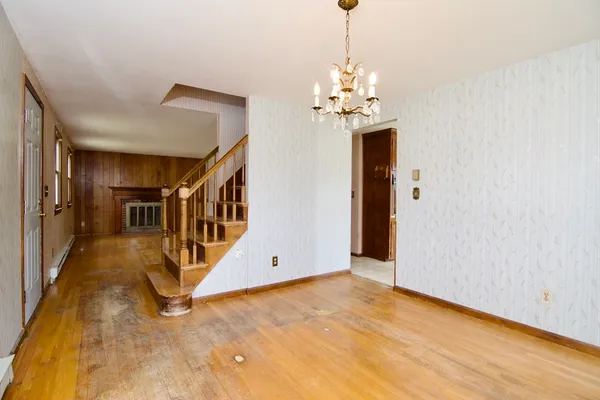 a view of an empty room with chandelier fan and wooden floor