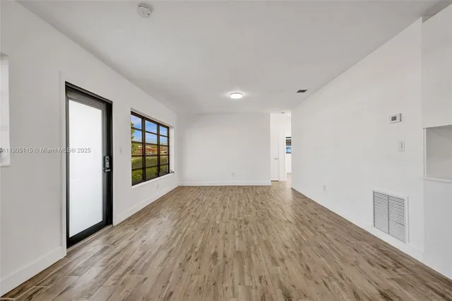a view of an empty room with wooden floor and a window