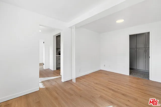 an empty room with wooden floor and way to kitchen