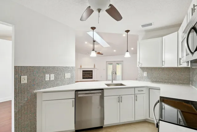 a kitchen with a sink dishwasher and white cabinets with wooden floor