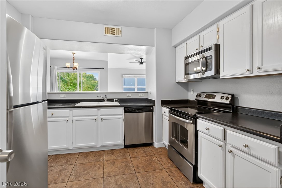 7255 West Sunset Road, Unit 2144 Las Vegas, NV 89113 - Photo 5 of 23 Kitchen with stainless steel appliances, white cabinets, dark countertops, and a chandelier