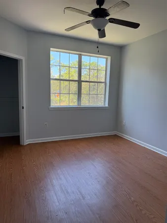 an empty room with wooden floor chandelier fan and windows