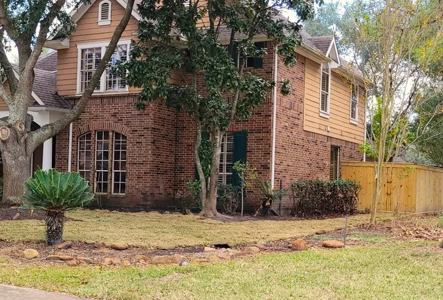 a view of a brick house with a yard and large tree